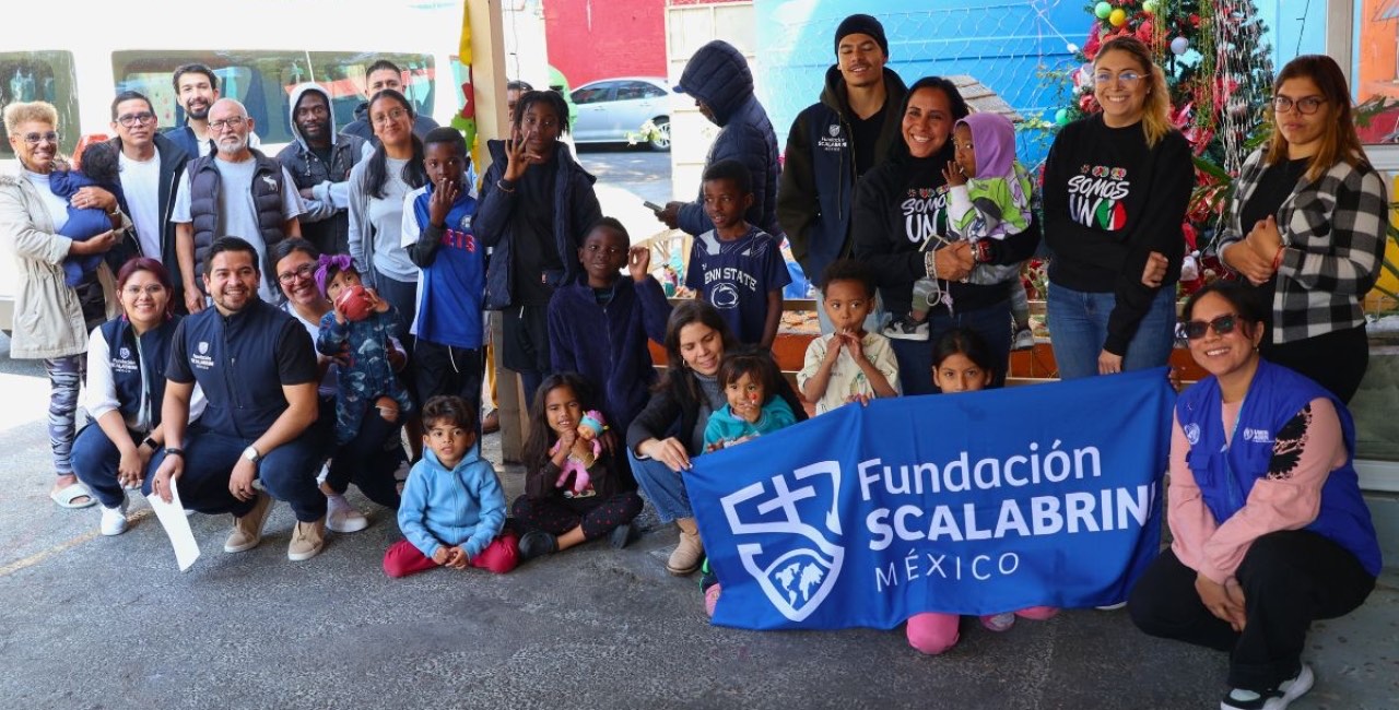 Equipo, voluntarios y familias migrantes posan juntos con la bandera de la Fundación Scalabrini México