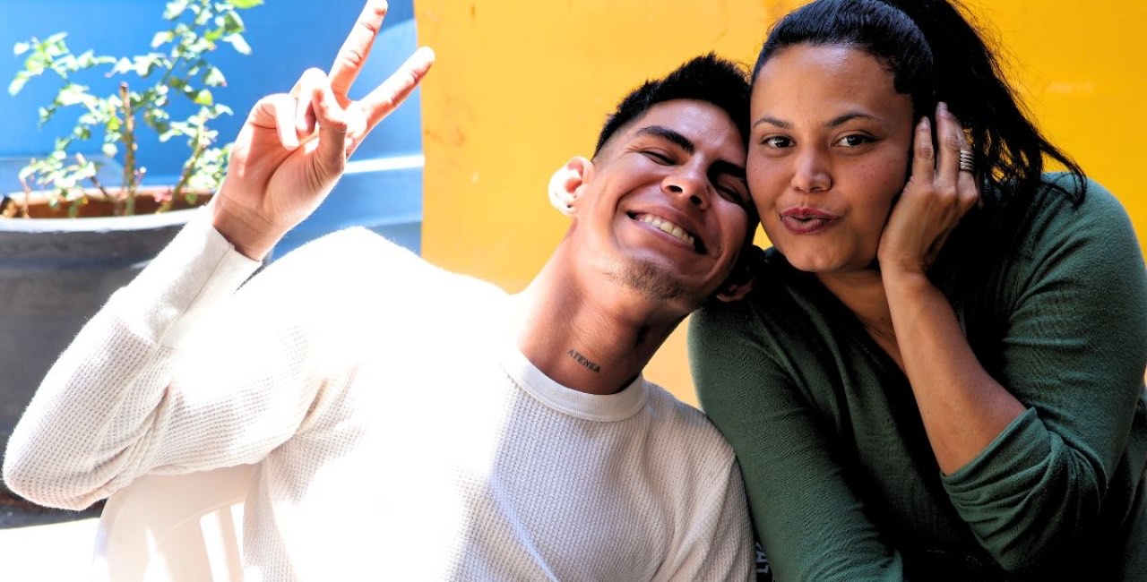 Un joven y una mujer sonríen abrazados en el patio de una casa de acogida