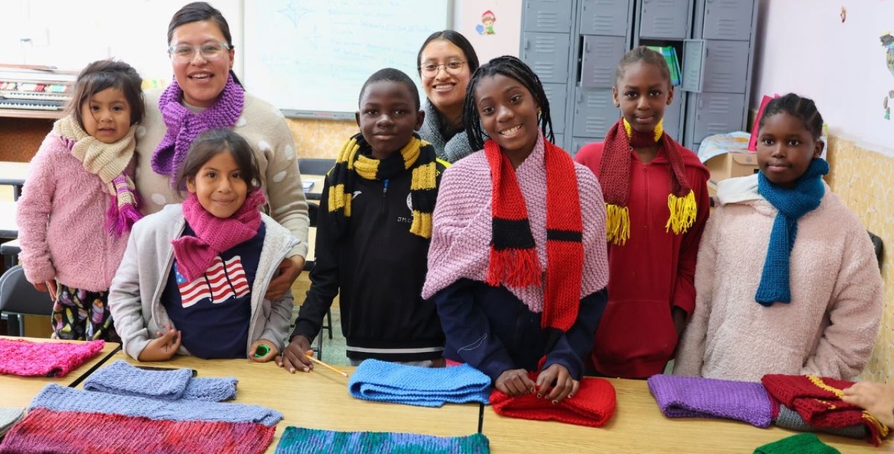 Niñas, niños y educadoras muestran las bufandas tejidas en un taller de una casa de acogida