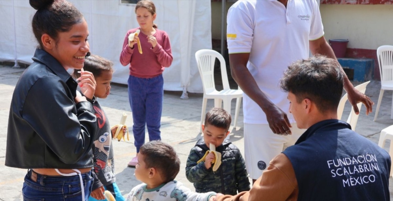 Un colaborador de la Fundación Scalabrini reparte fruta a niñas, niños y sus familias en el patio de una casa