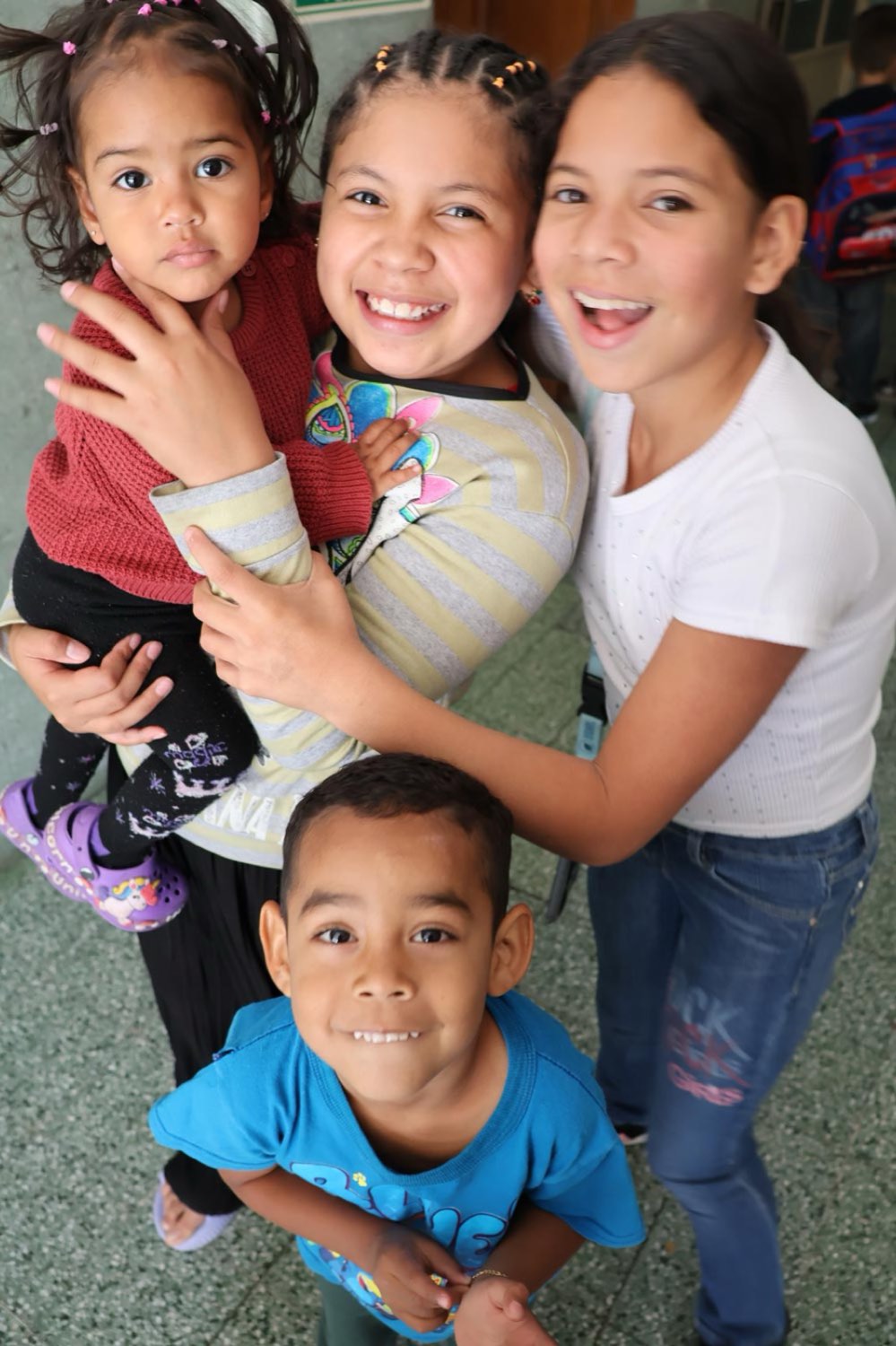 Niñas y niños abrazados sonríen en el patio de la casa