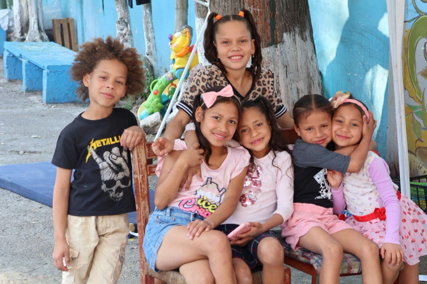 Niñas y niños sonríen sentados juntos en el patio de una de las casas